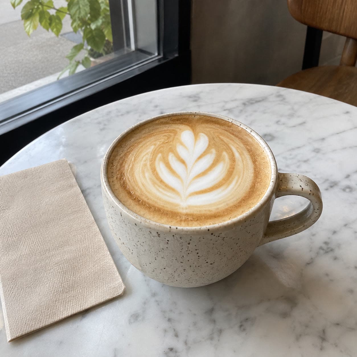 A latte with a leaf in the foam on a marble cafe table.